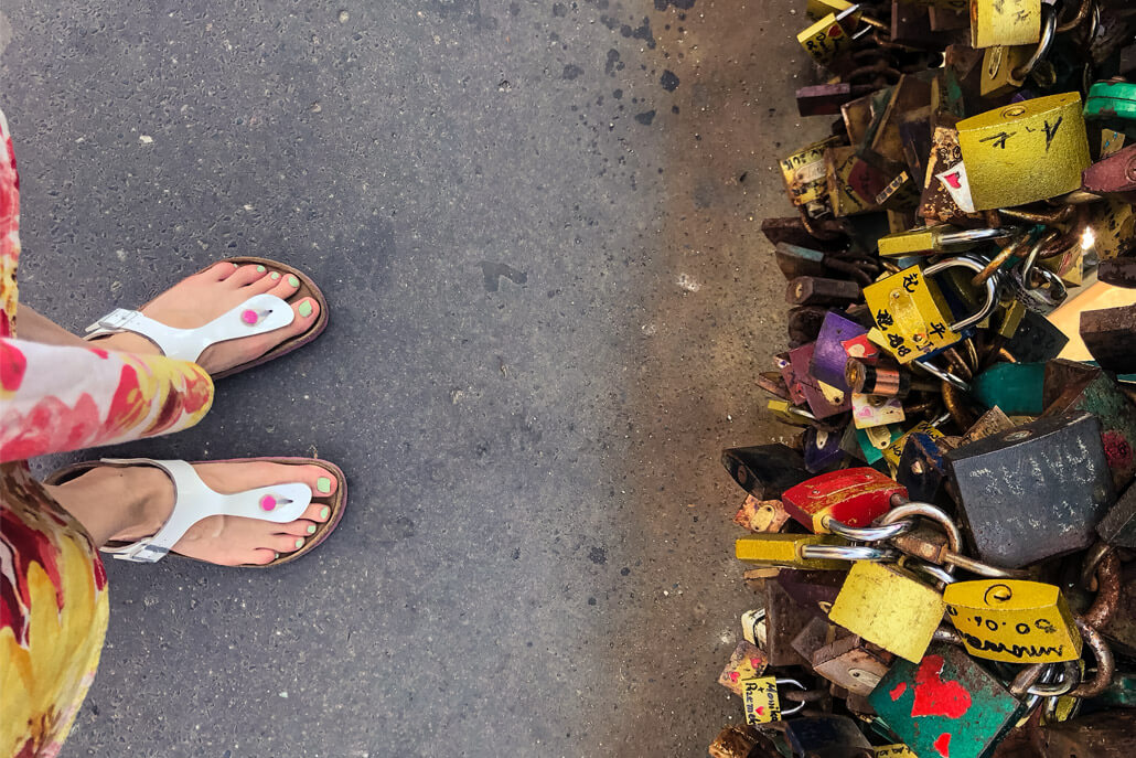 Closeup of feet in flip flops with love locks on a bridge