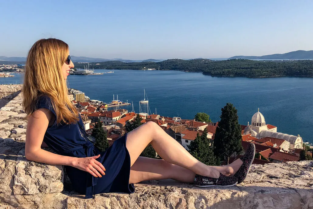 A woman sitting on a wall with a view of Sibenik City, Croatia