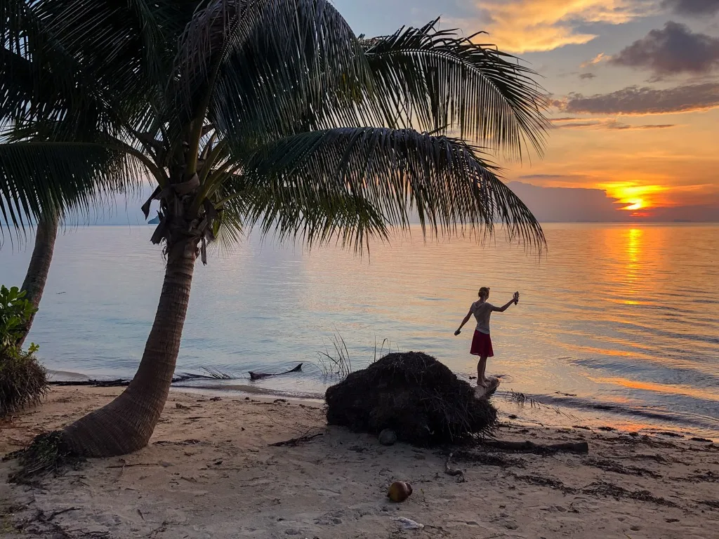 A woman standing on a palm trunk on a beach in Thailand upon sunset (Hinkong Beach, Koh Phangan)