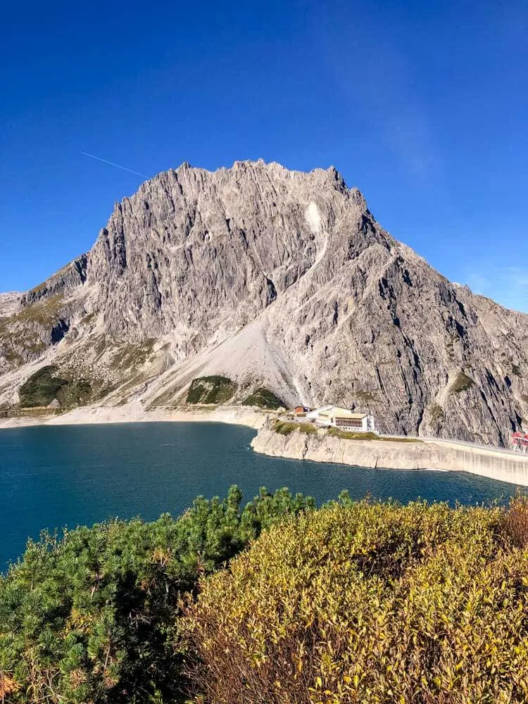 An alpine hut on a lake shore with a mountain behind