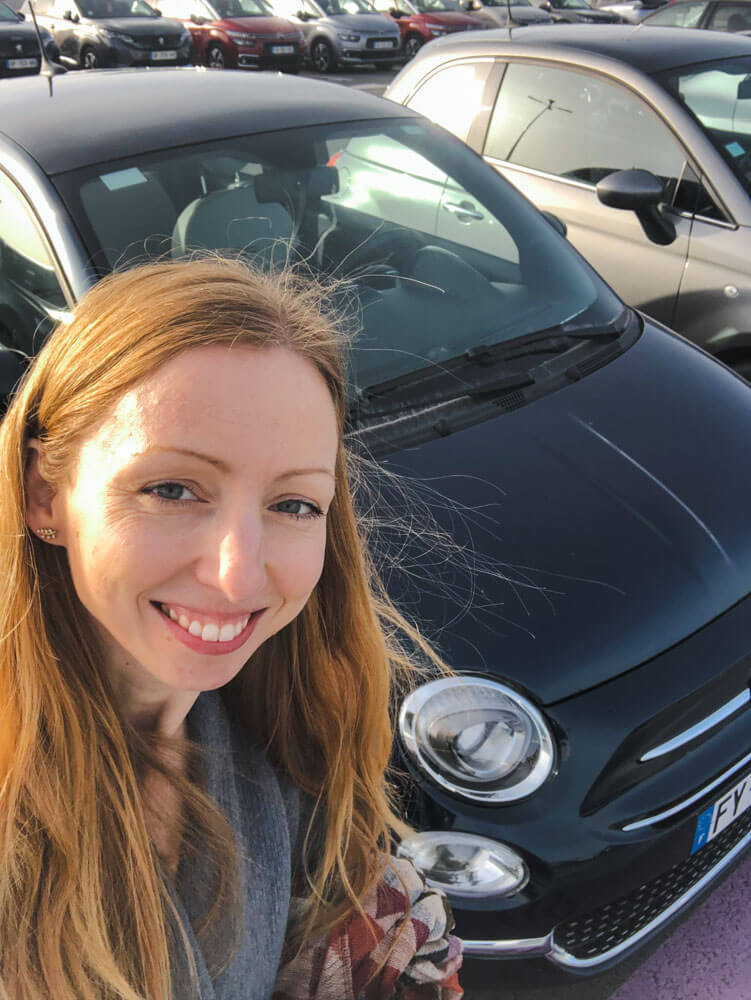 Veronika of TravelGeekery taking a selfie with her rental car in France