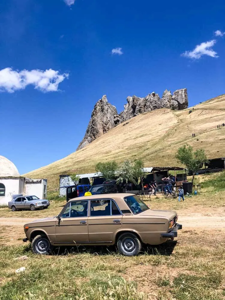 An old Soviet-made car parked below a landmark in Azerbaijan