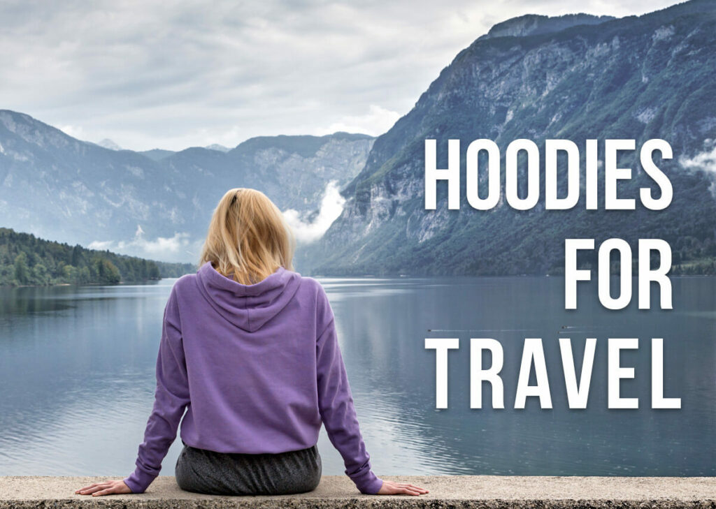 A woman sitting by a lake with her back towards us with a text overlay: Hoodies for Travel