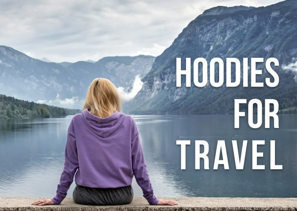 A woman sitting by a lake with her back towards us with a text overlay: Hoodies for Travel