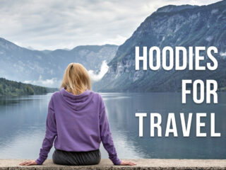 A woman sitting by a lake with her back towards us with a text overlay: Hoodies for Travel