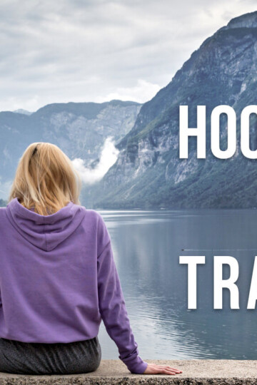 A woman sitting by a lake with her back towards us with a text overlay: Hoodies for Travel