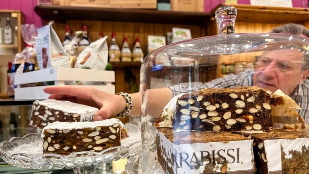 A small vendor in Siena is serving a piece of Panforte, local dessert.