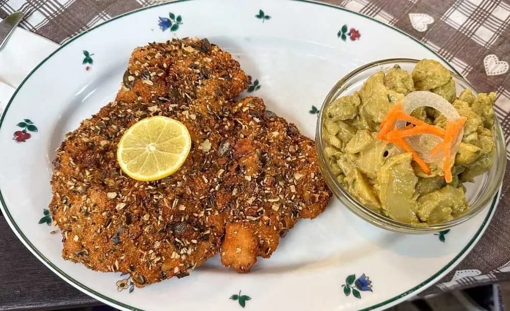 View of a plate with a schnitzel covered in pumpkin seeds and potatoes with a green dressing