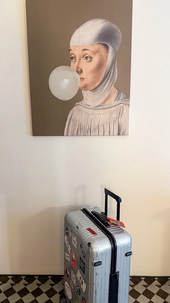 A funky painting in a hotel with a suitcase placed below.