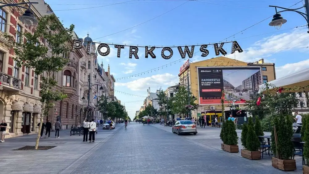 A wide boulevard in Lodz, Poland, with the Piotrkowska sign hanging in the middle on a sunny day