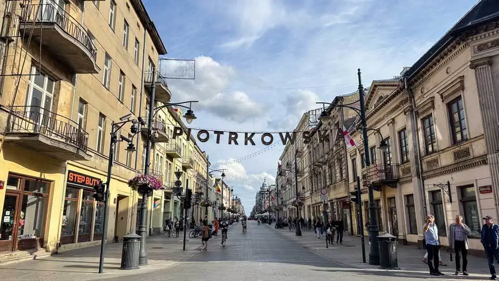 A wide boulevard with a large sign Piotrkowska hanging in the middle