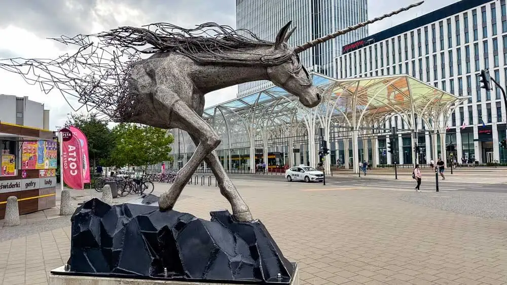 a statue of a unicorn in front of a tram stop with pastel-colored roof in Lodz, Poland