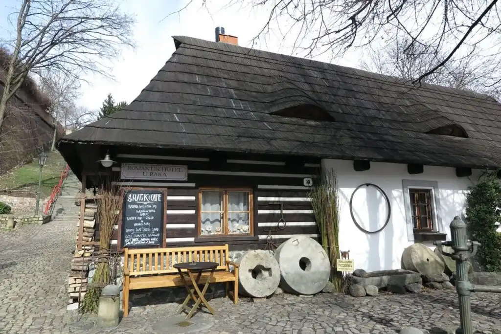 Traditional wooden building with a steep dark roof and stone mill wheels, housing the Romantik Hotel U Raka in Prague.