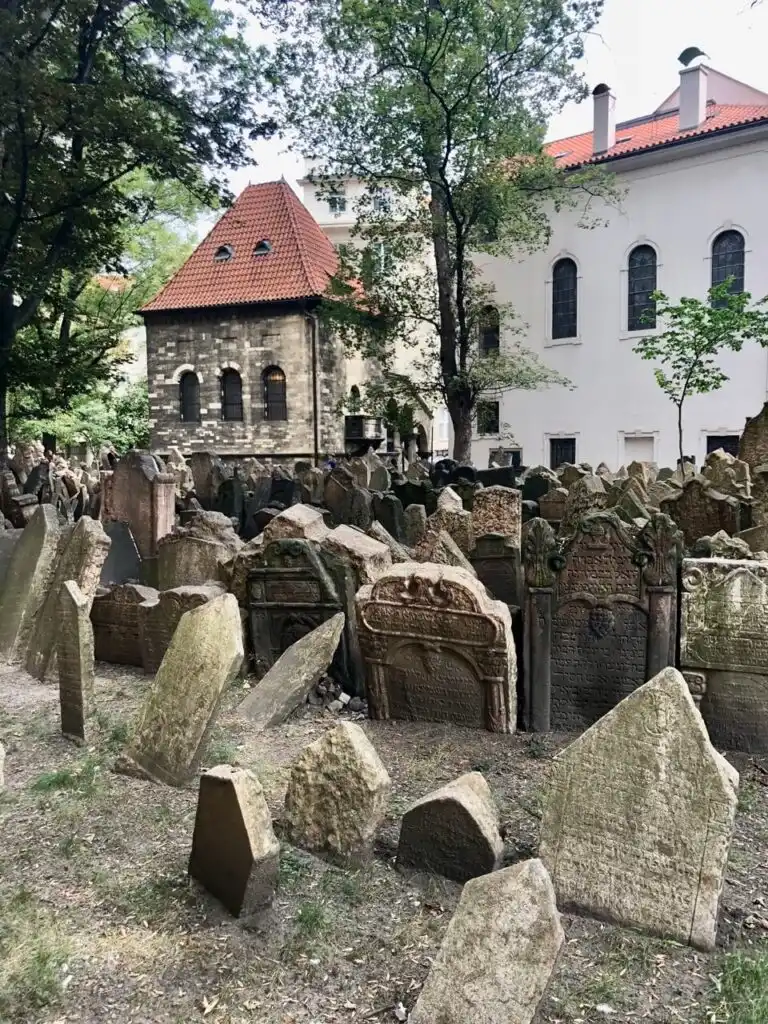 Dense grouping of ancient, weathered headstones in the Old Jewish Cemetery with historical stone buildings in the background