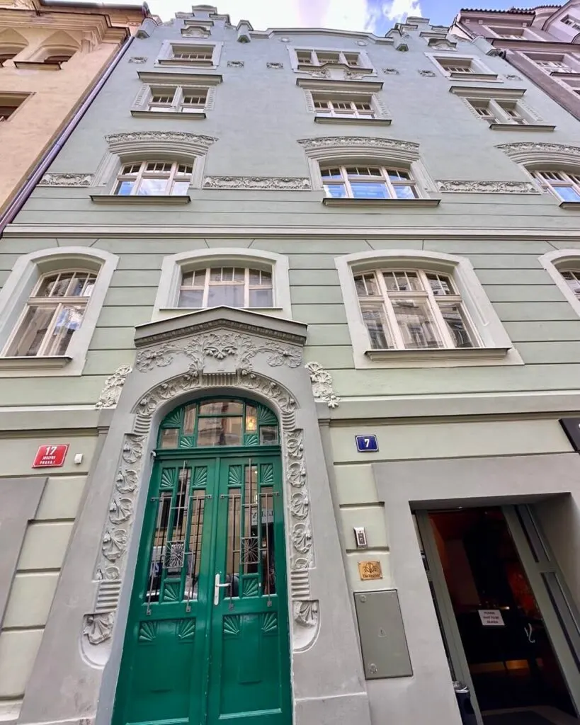 Pale green Art Nouveau building in Prague with intricate floral details around windows and a green arched front door.