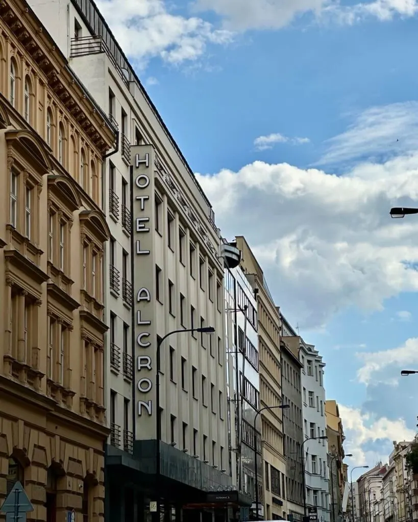 Street view of Hotel Alcron’s vertical sign on a mid-century modern building in central Prague, surrounded by historic facades.