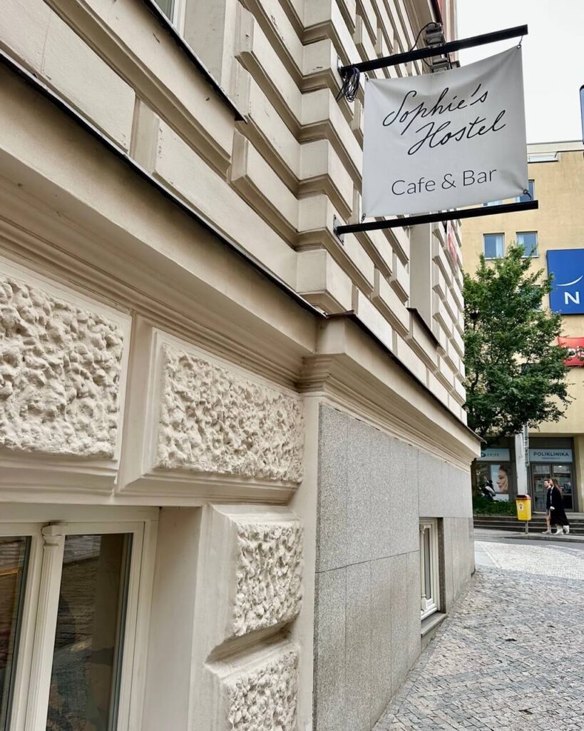 Close-up of Sophie's Hostel sign reading “Café & Bar” on the side of a cream-colored stone building in Prague.