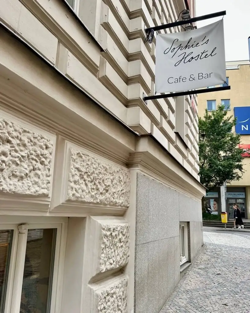 Close-up of Sophie's Hostel sign reading “Café & Bar” on the side of a cream-colored stone building in Prague.