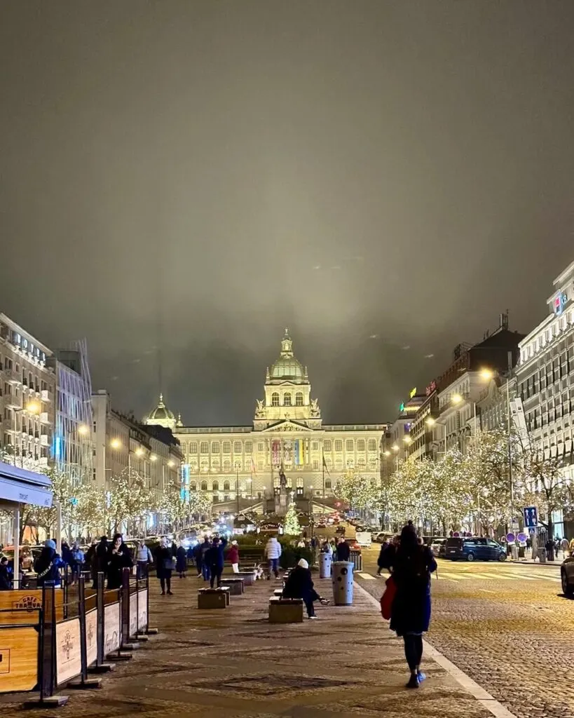 Wenceslas Square illuminated at night with string lights and the National Museum glowing at the far end.