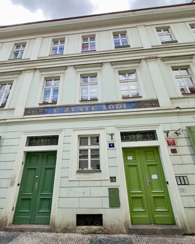 Pale mint-green historic building with two green doors and a blue-and-gold sign reading "U Zlaté Lodi" above.