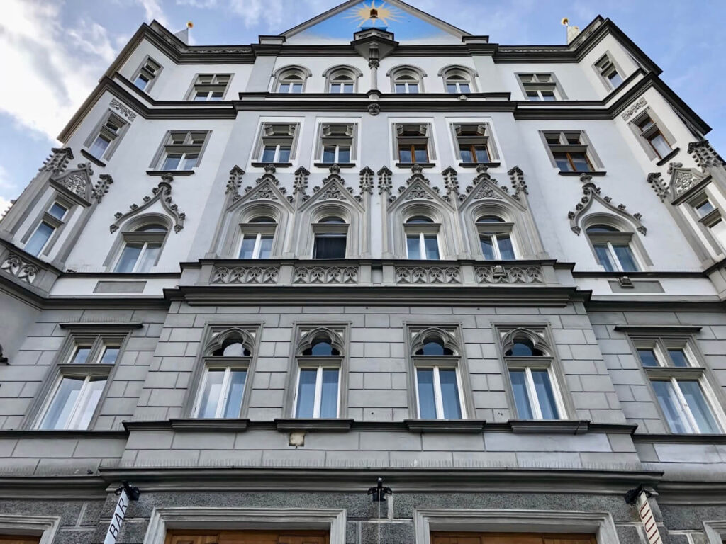 Dramatic gray-and-white facade with ornate pointed arches, tracery windows, and decorative stonework in central Prague.