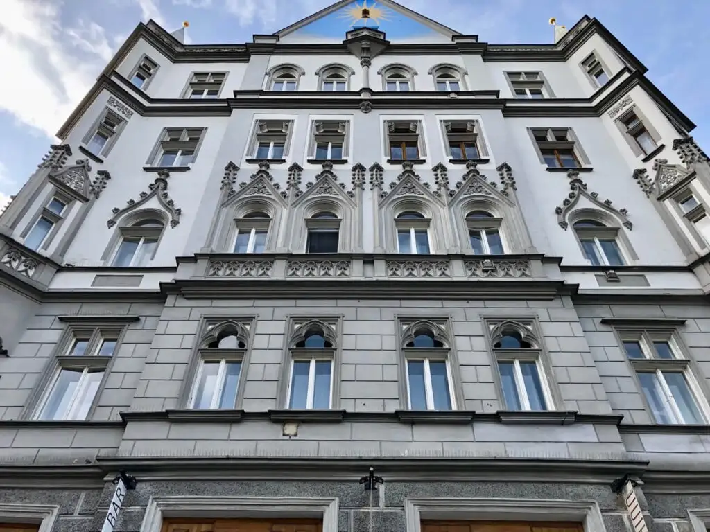 Dramatic gray-and-white facade with ornate pointed arches, tracery windows, and decorative stonework in central Prague.