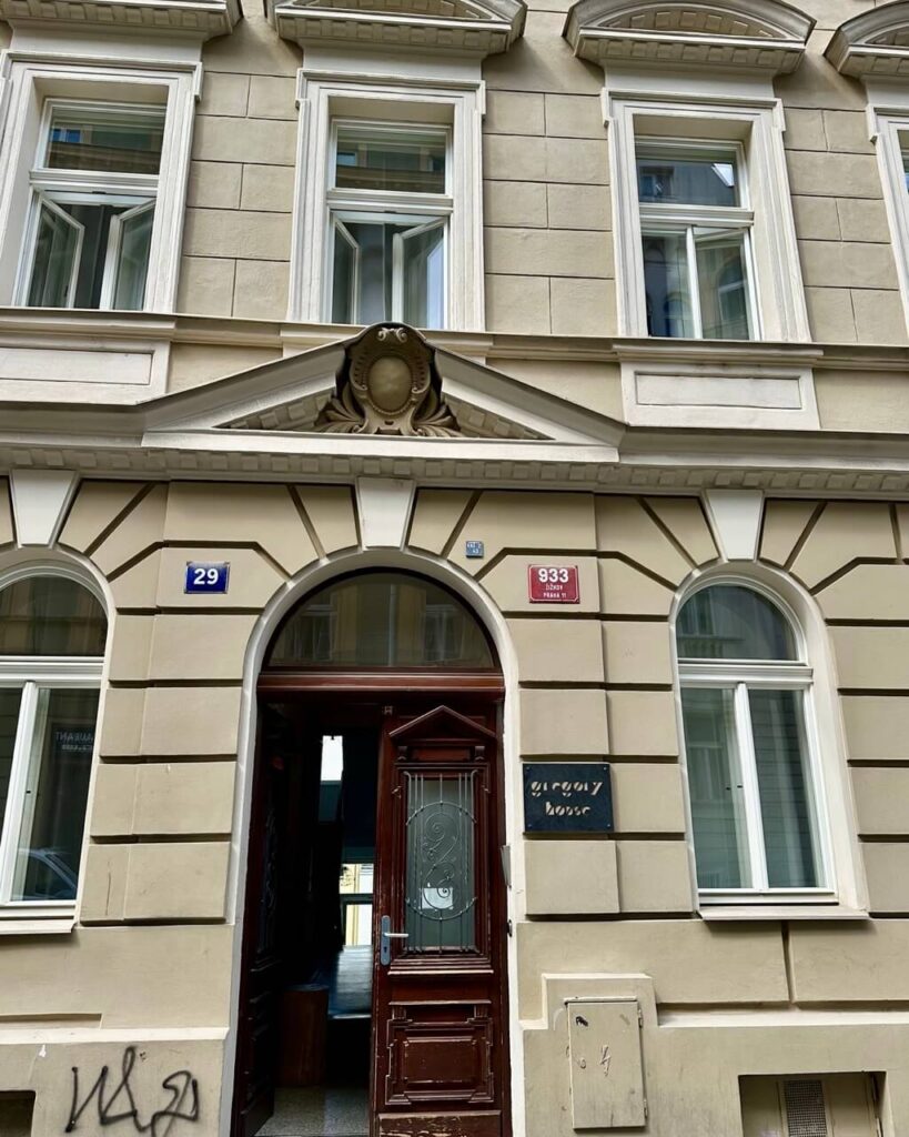 Ornate brown doorway of Gregory House, a beige classic building with white-trimmed windows and street number plaques in Prague.