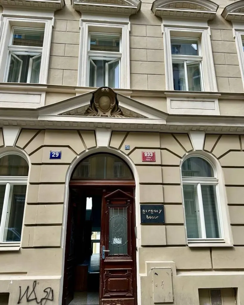Ornate brown doorway of Gregory House, a beige classic building with white-trimmed windows and street number plaques in Prague.