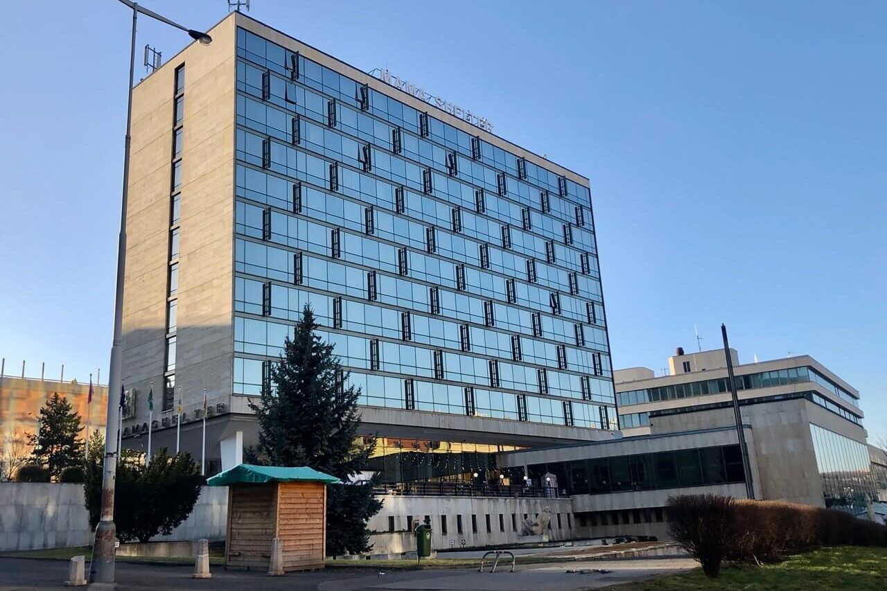 Exterior shot of Mama Shelter Prague taken from a distance, showing the full height of the modern glass building under clear skies.