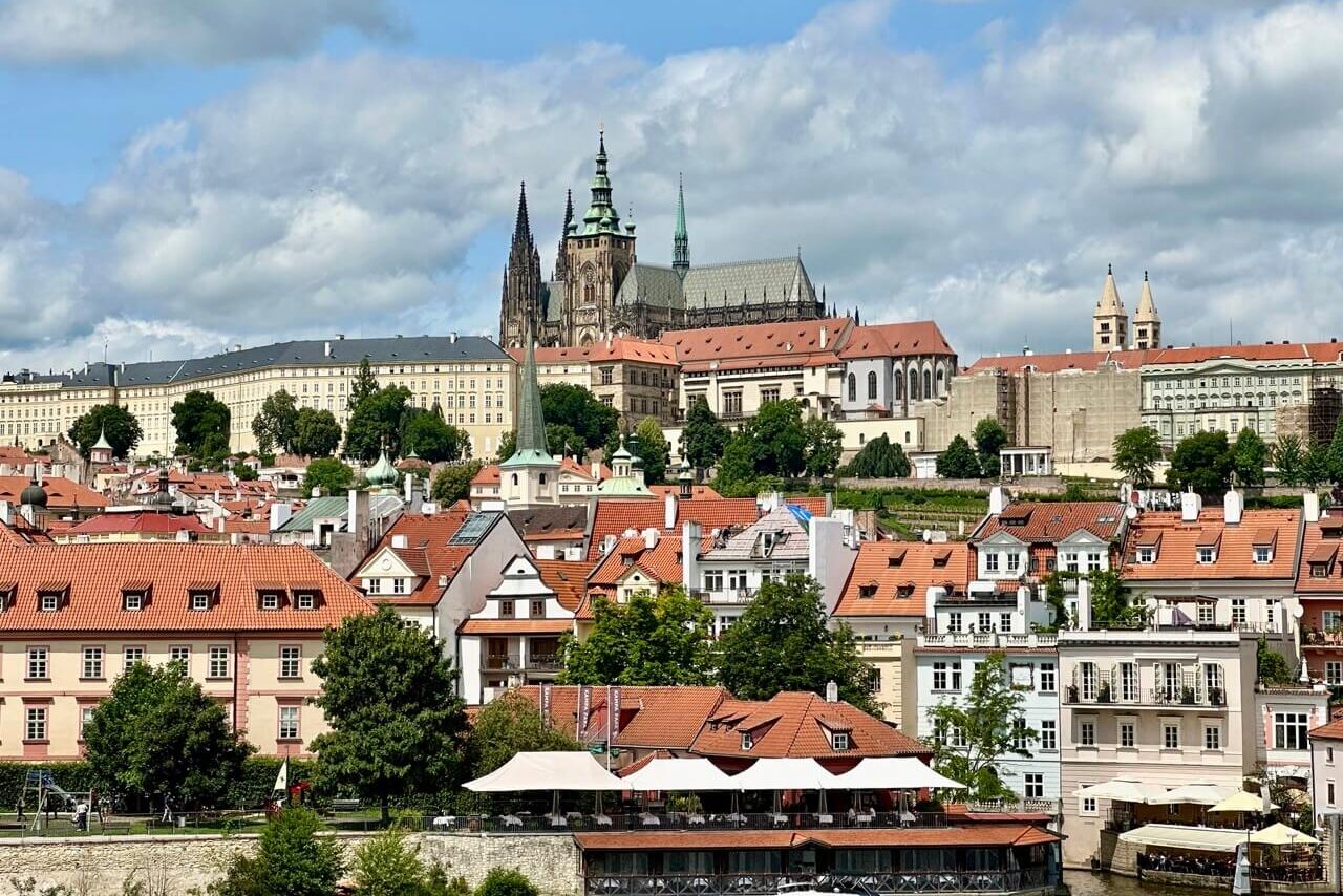 Panoramic view of Prague Castle and St. Vitus Cathedral overlooking red-roofed buildings in the historic Malá Strana district.