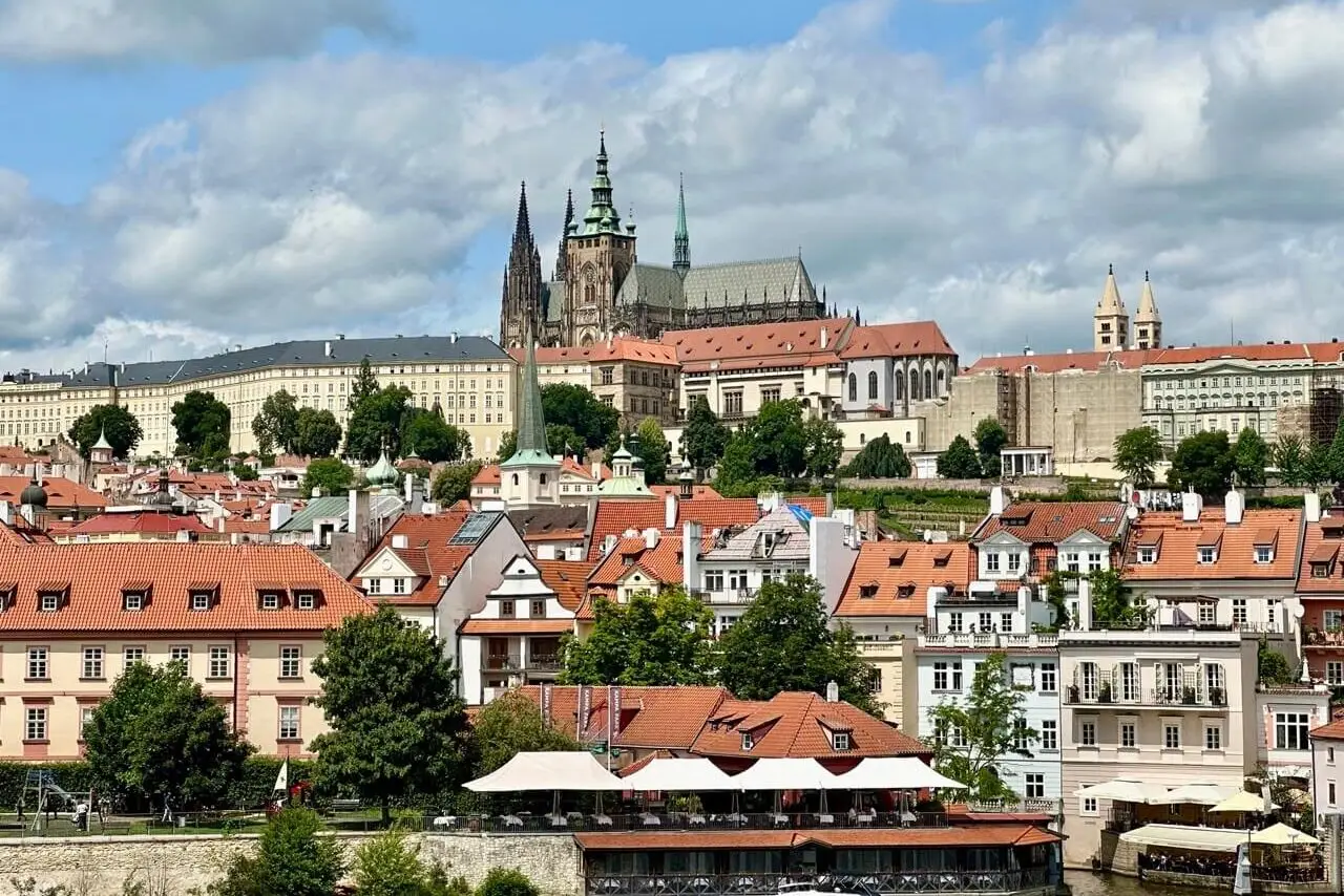 Panoramic view of Prague Castle and St. Vitus Cathedral overlooking red-roofed buildings in the historic Malá Strana district.