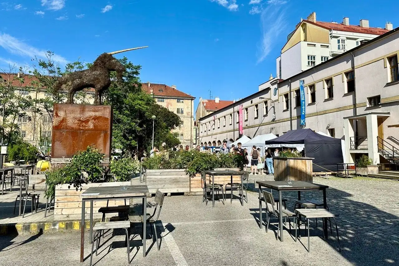 Outdoor courtyard of Kasárna Karlín in Prague featuring a large unicorn sculpture, café seating, and market tents.