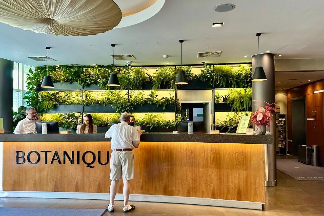 Front desk area of Hotel Botanique featuring a wooden counter, vertical plant wall, and warm modern lighting.