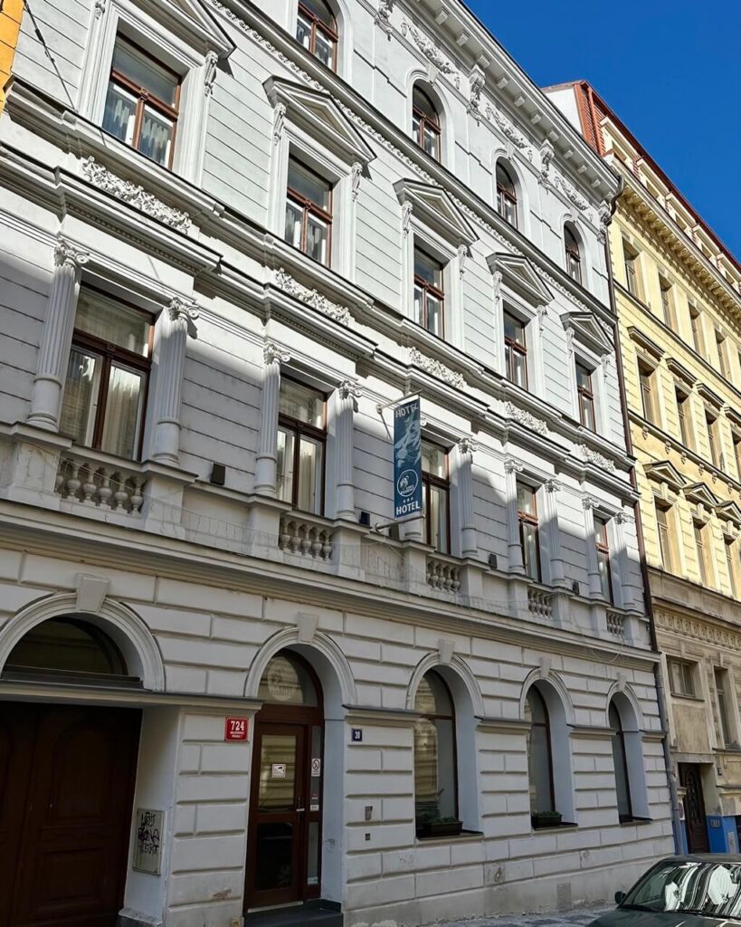 White historic building with arched doorways, decorative window frames, and a vertical sign reading “Kings Residence Hotel” in Prague.