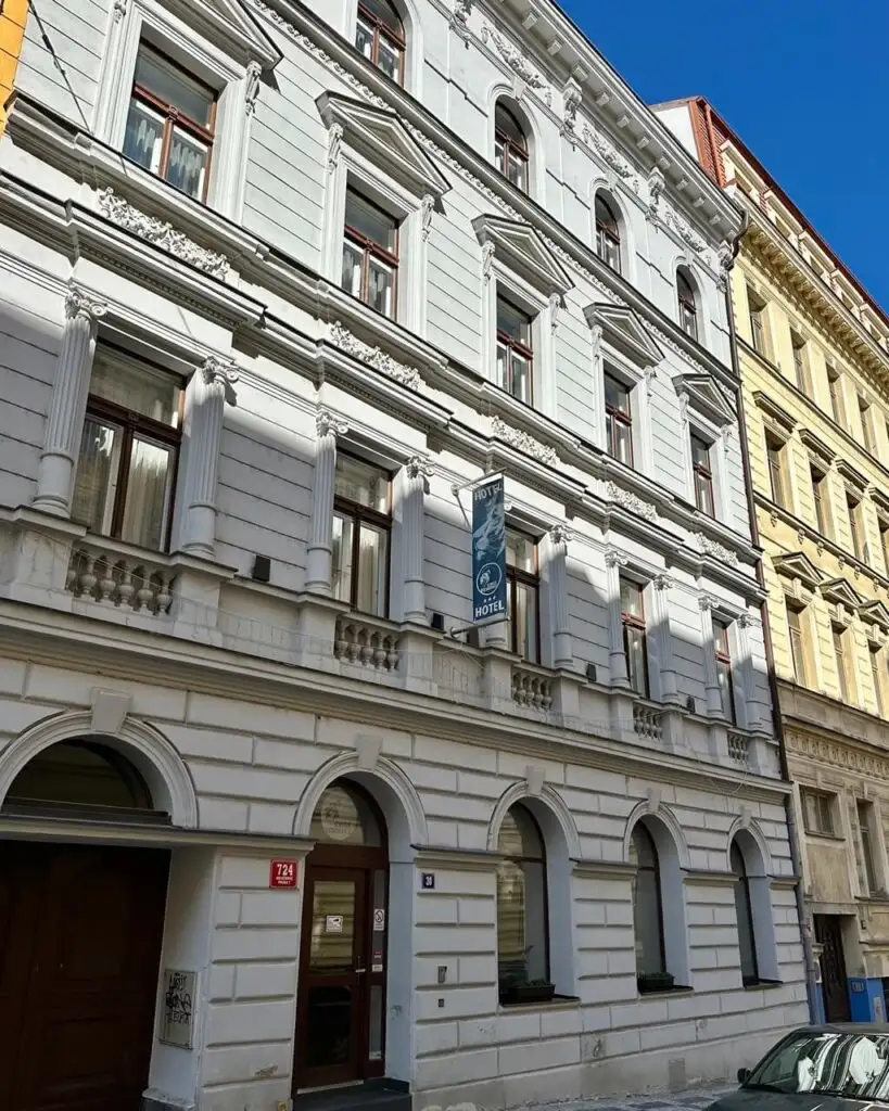 White historic building with arched doorways, decorative window frames, and a vertical sign reading “Kings Residence Hotel” in Prague.