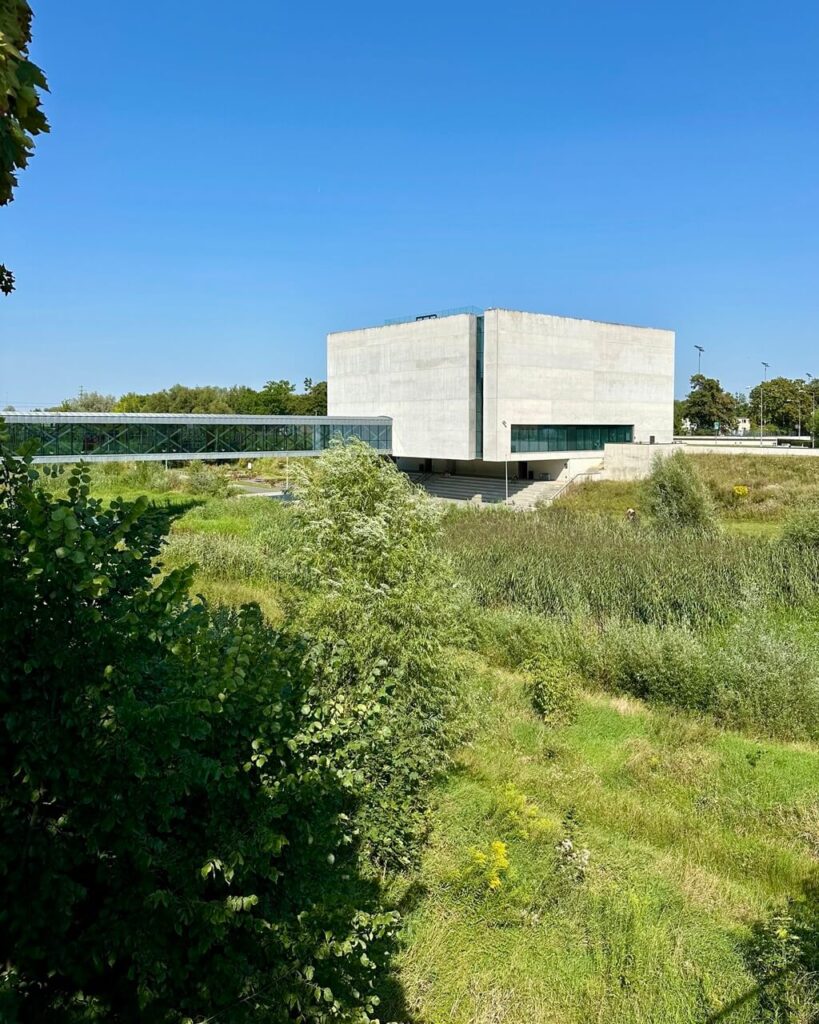 A modern concrete building surrounded by greenery under a bright blue sky.