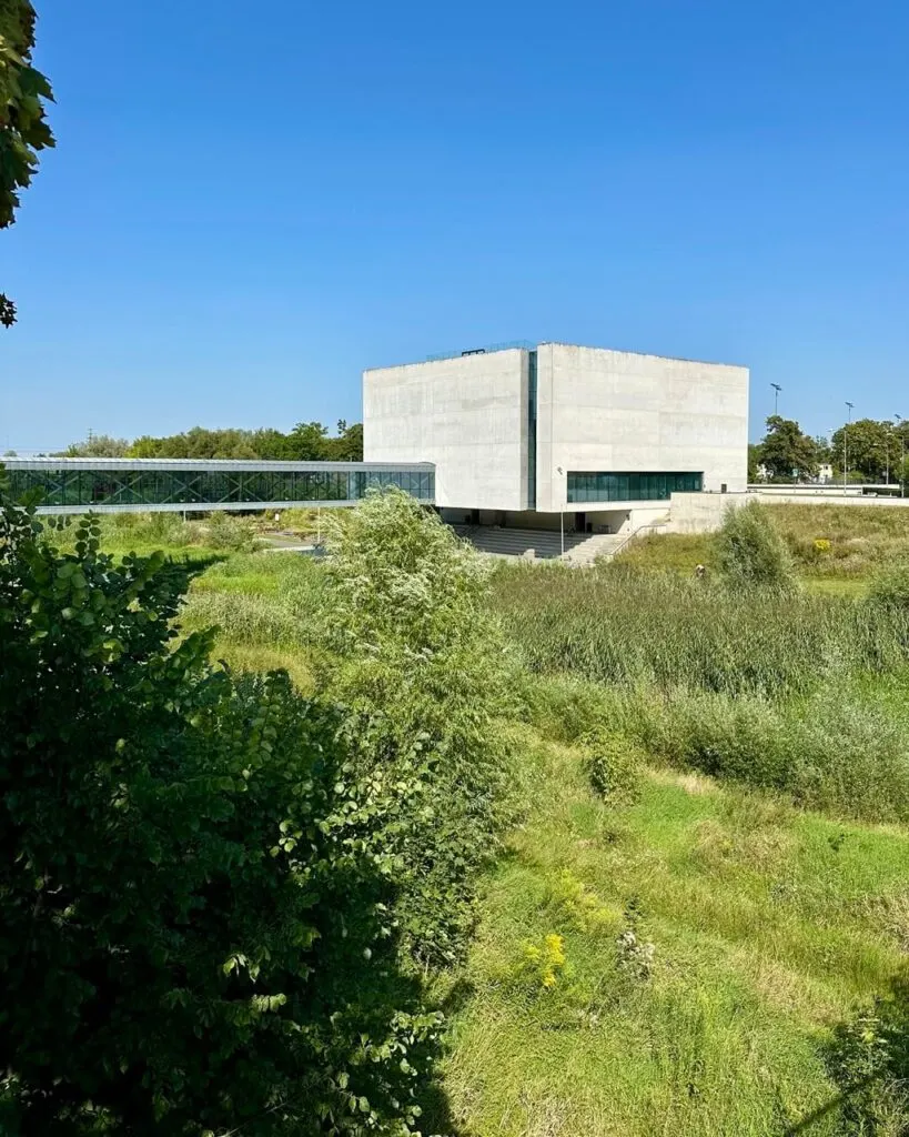 A modern concrete building surrounded by greenery under a bright blue sky.