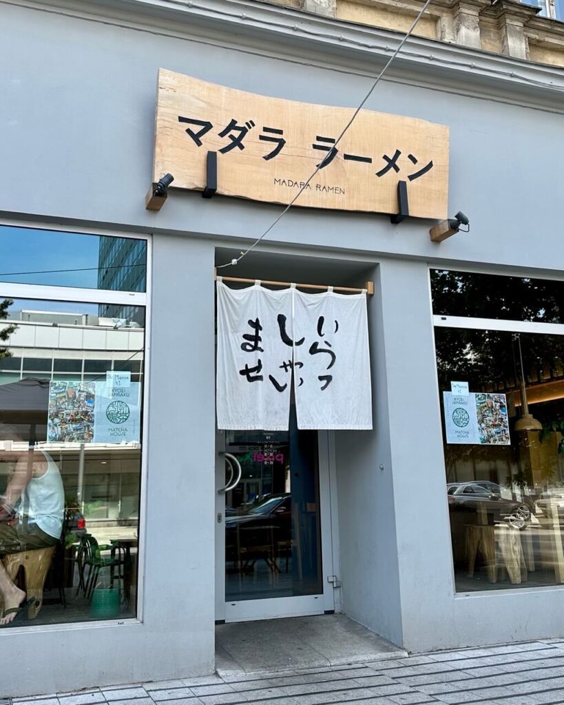 Exterior of Madara Ramen with Japanese signage and a white curtain entrance.