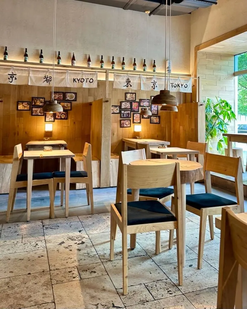 Minimalist Japanese-style interior with light wooden furniture, booth seating, and hanging lanterns.