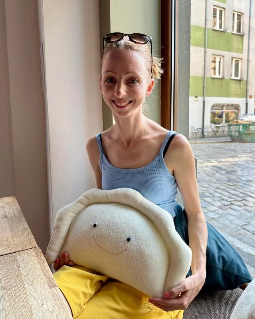 Woman smiling at the camera while holding a plush toy shaped like a smiling pierogi.