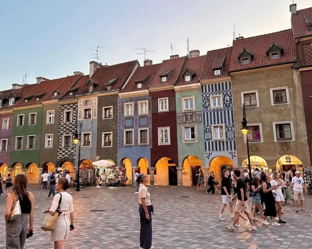 Tourists walk through Poznan Old Market Square past a row of colorful, narrow townhouses with intricate facades.