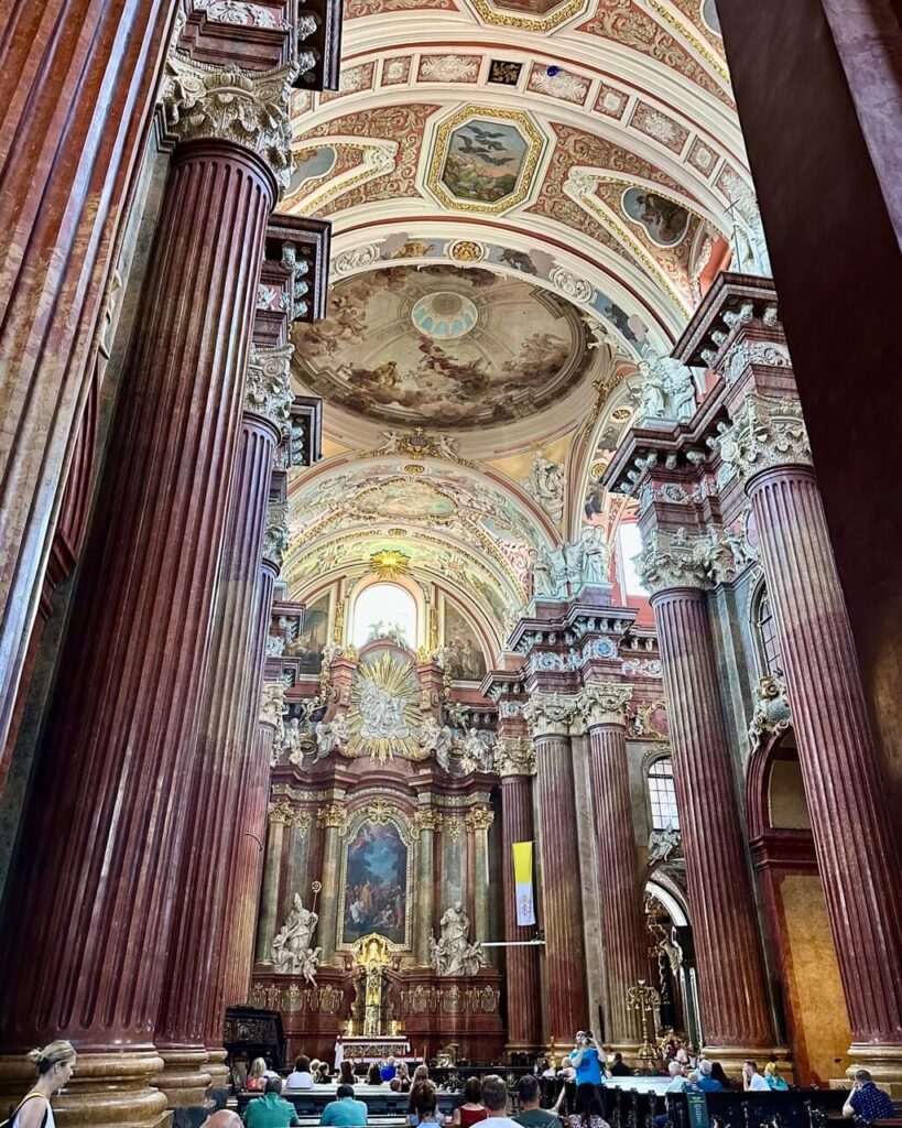Ornate Baroque church interior with massive red marble columns and a frescoed ceiling.