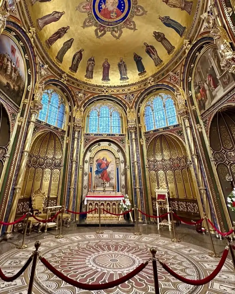 Ornate chapel interior with golden domed ceiling, red rope barriers, and religious paintings.
