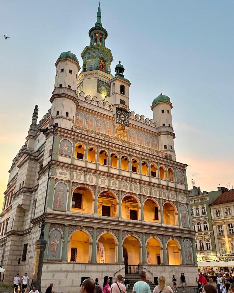 Poznan Town Hall lit warmly at dusk, with people gathered in the Old Market Square below.