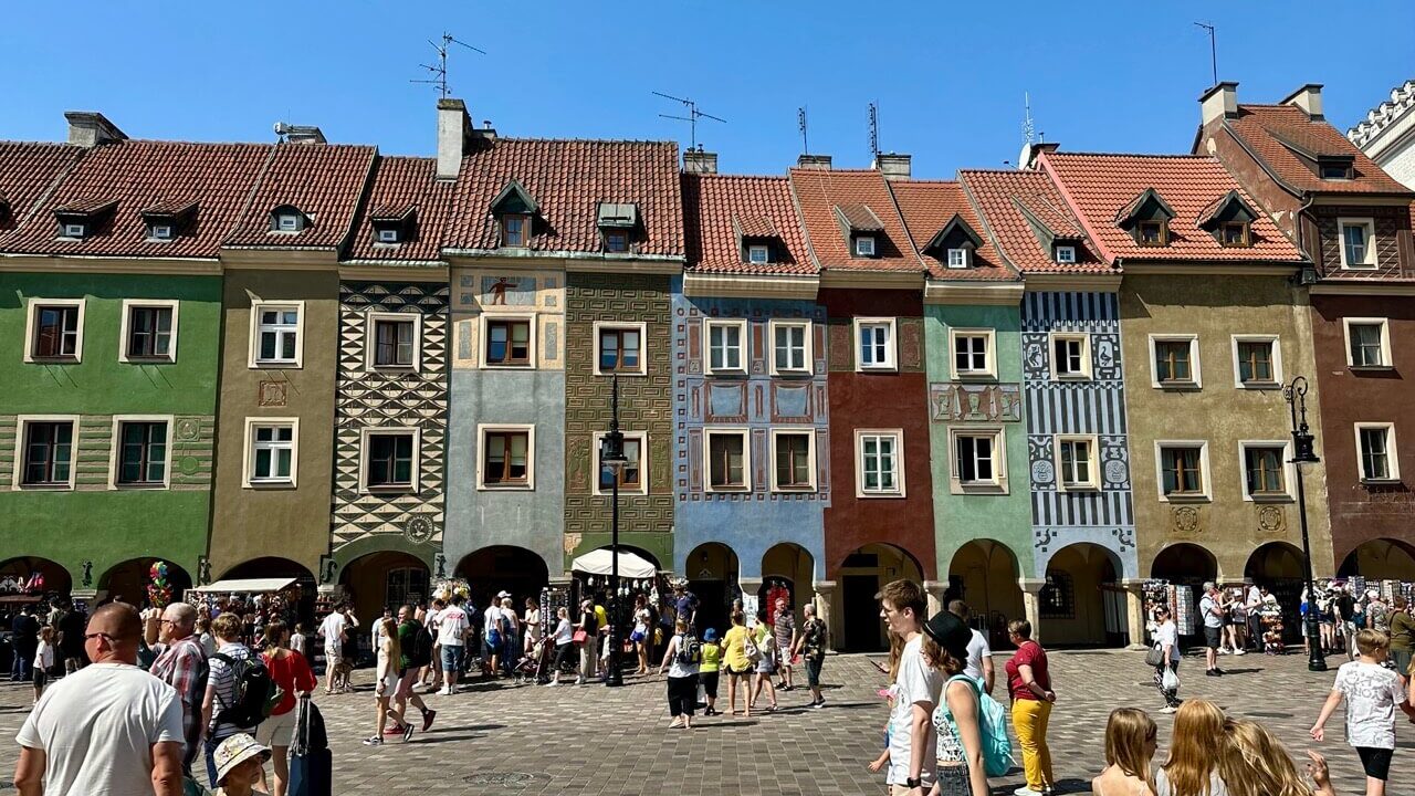 Colorful row of historic townhouses with red roofs in the Old Market Square, crowded with people.