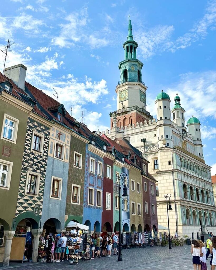 View of Poznan Town Hall tower rising above a row of ornately painted buildings with souvenir stalls below.