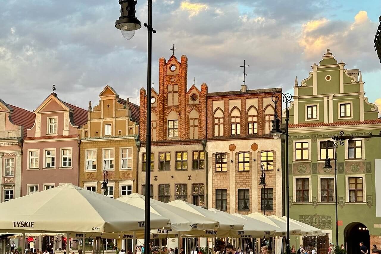 Café diners sit beneath umbrellas near a row of colorful townhouses in Poznan’s Old Town at sunset.