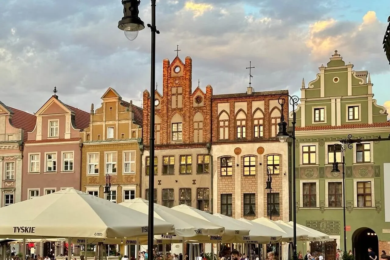 Café diners sit beneath umbrellas near a row of colorful townhouses in Poznan’s Old Town at sunset.