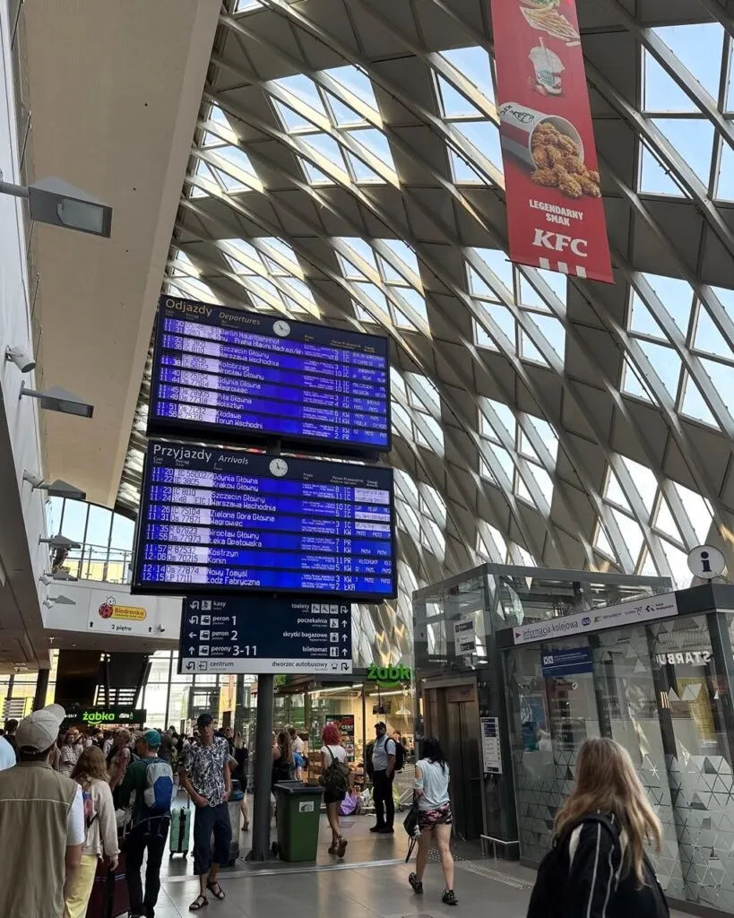 Large digital departure and arrival boards hang above a busy hallway in Poznan’s main train station.