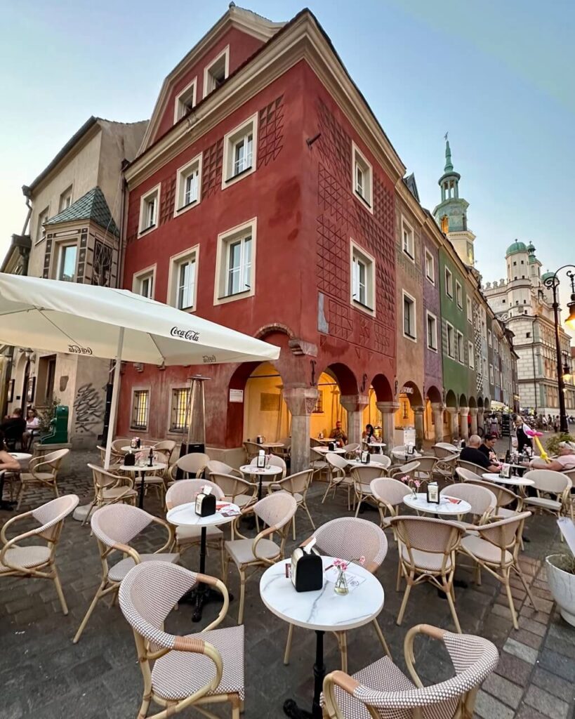 Outdoor café seating lines a cobblestone alley beside a red historic building near Poznan Town Hall.